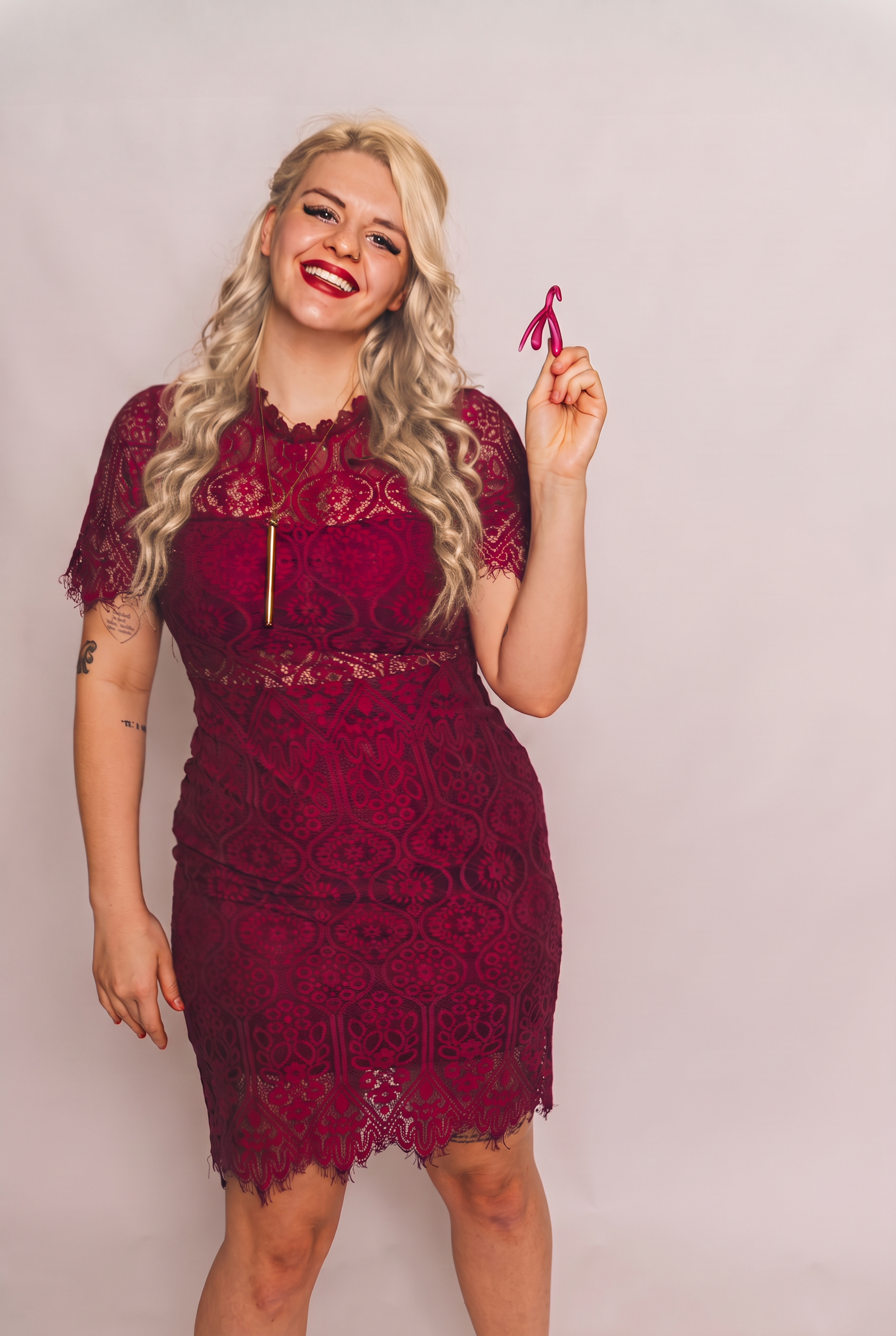 Dr. Amber Mallery laughing in a burgundy lace dress while holding up a pink clitoris anatomy model